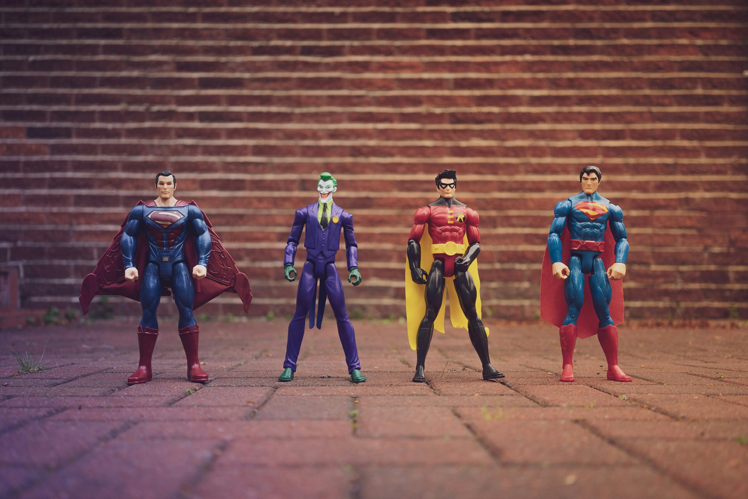 Four action figures stand in a row on a brick surface, with a staircase in the background.