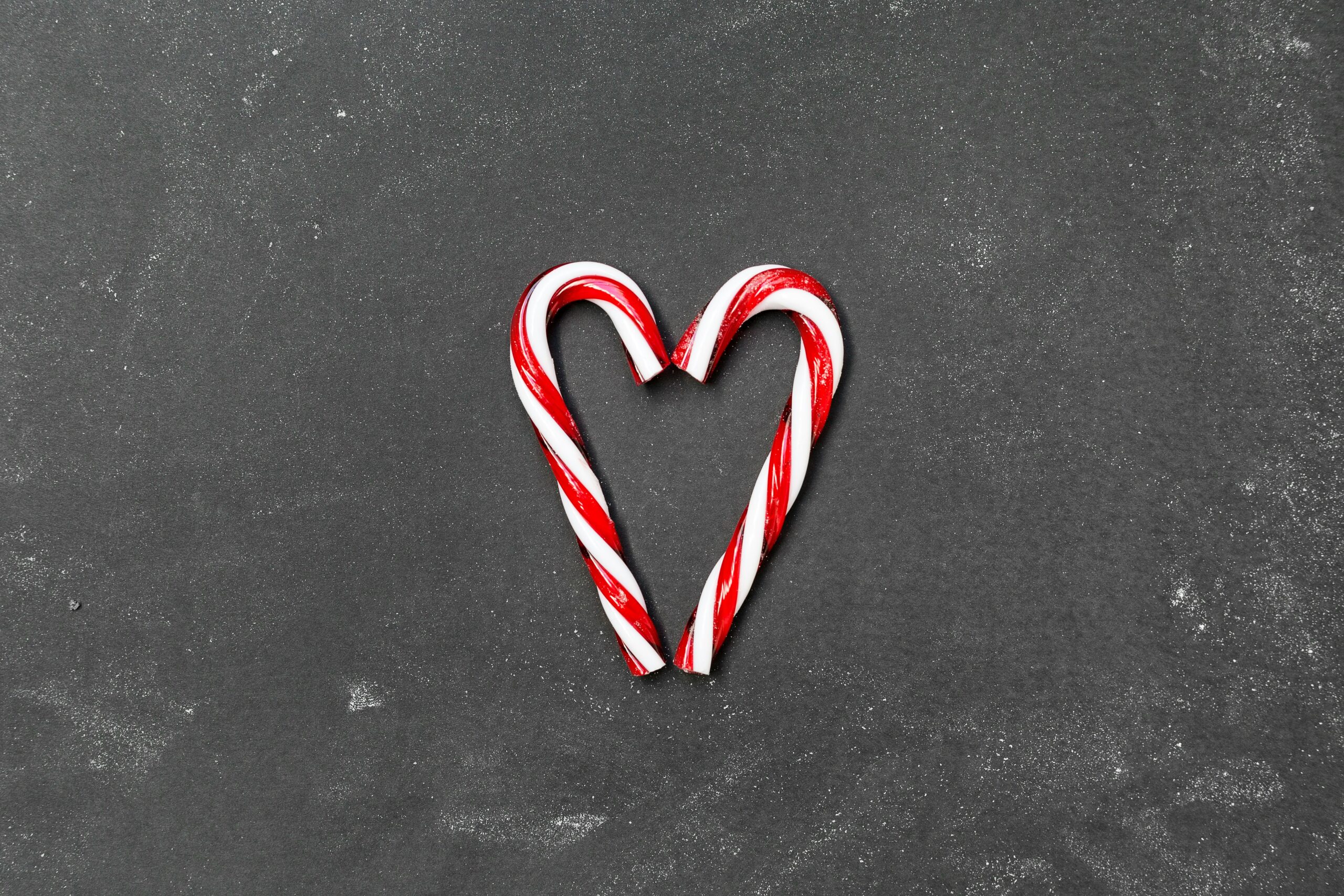 Two candy canes forming a heart shape on a dark gray background.