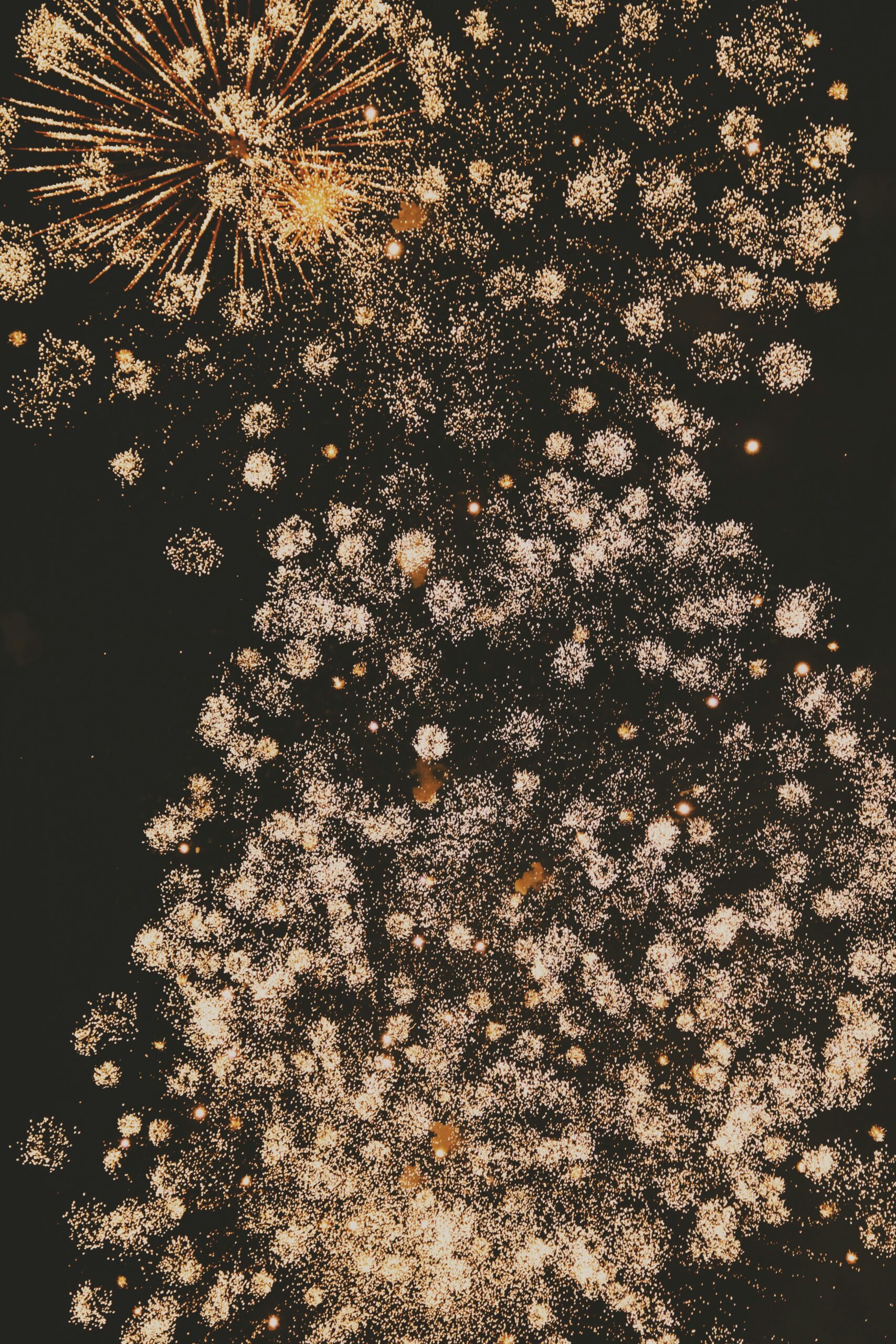 A night sky filled with numerous golden fireworks bursting, creating bright, sparkling patterns against a dark background.