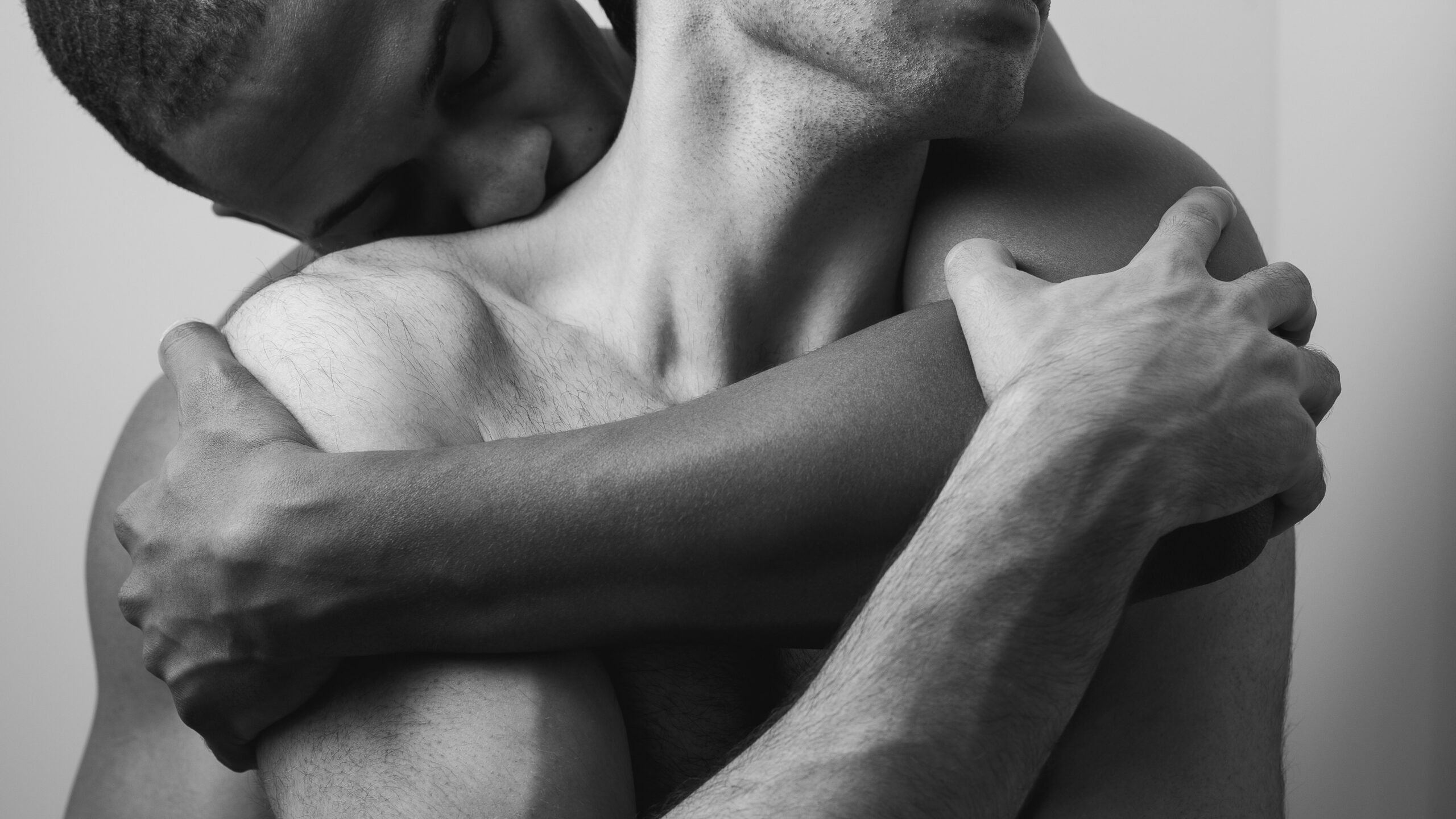 Two individuals embrace closely in a black-and-white photograph, one person kissing the other's neck.